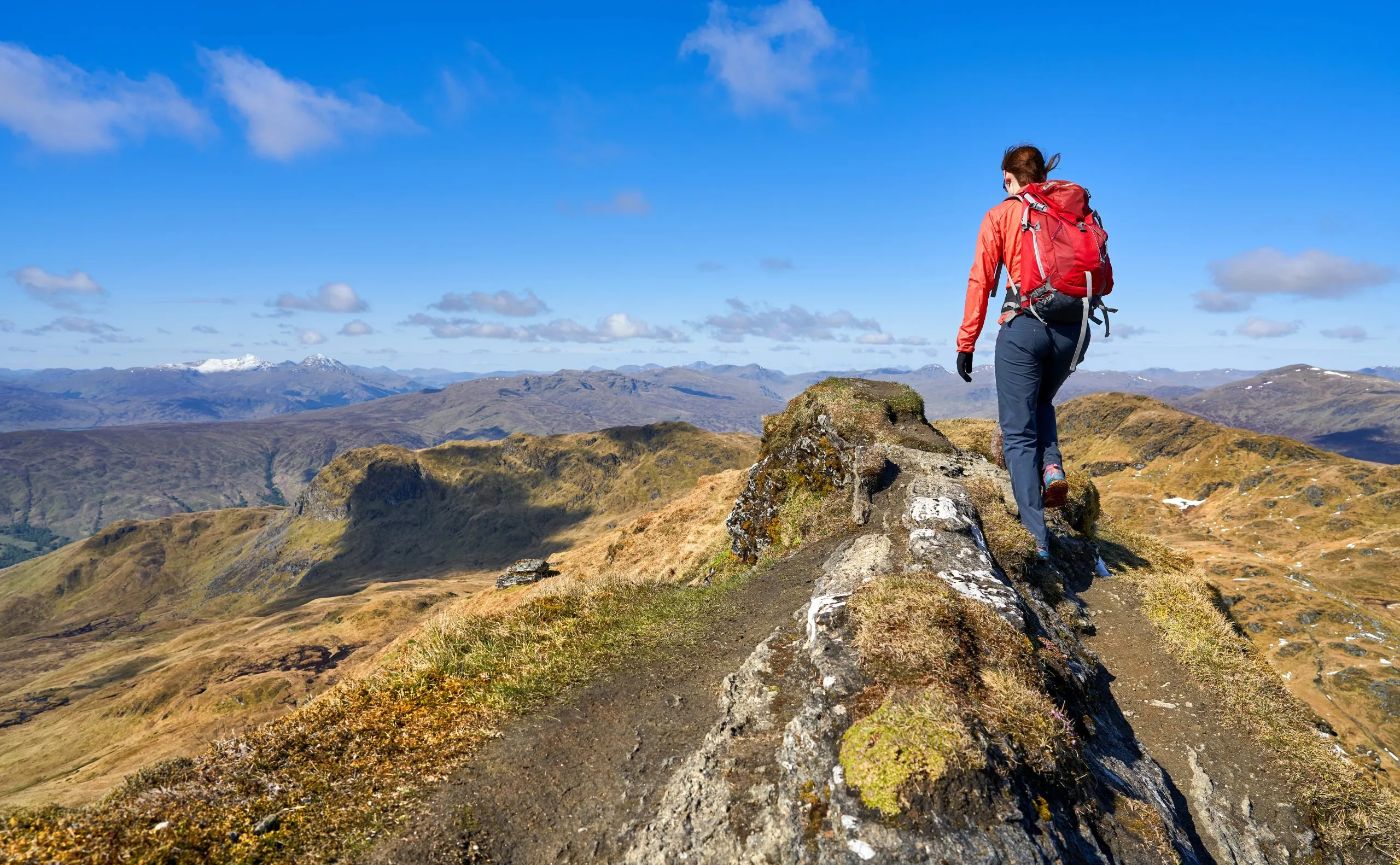 A hiker walking over the mountain summit ridge of Meall Garbh towards the top of Beinn nan Eachan in the Scottish Highlands, UK Landscapes.